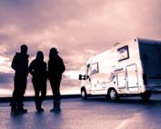 group of three people beside an RV under a cloudy sky